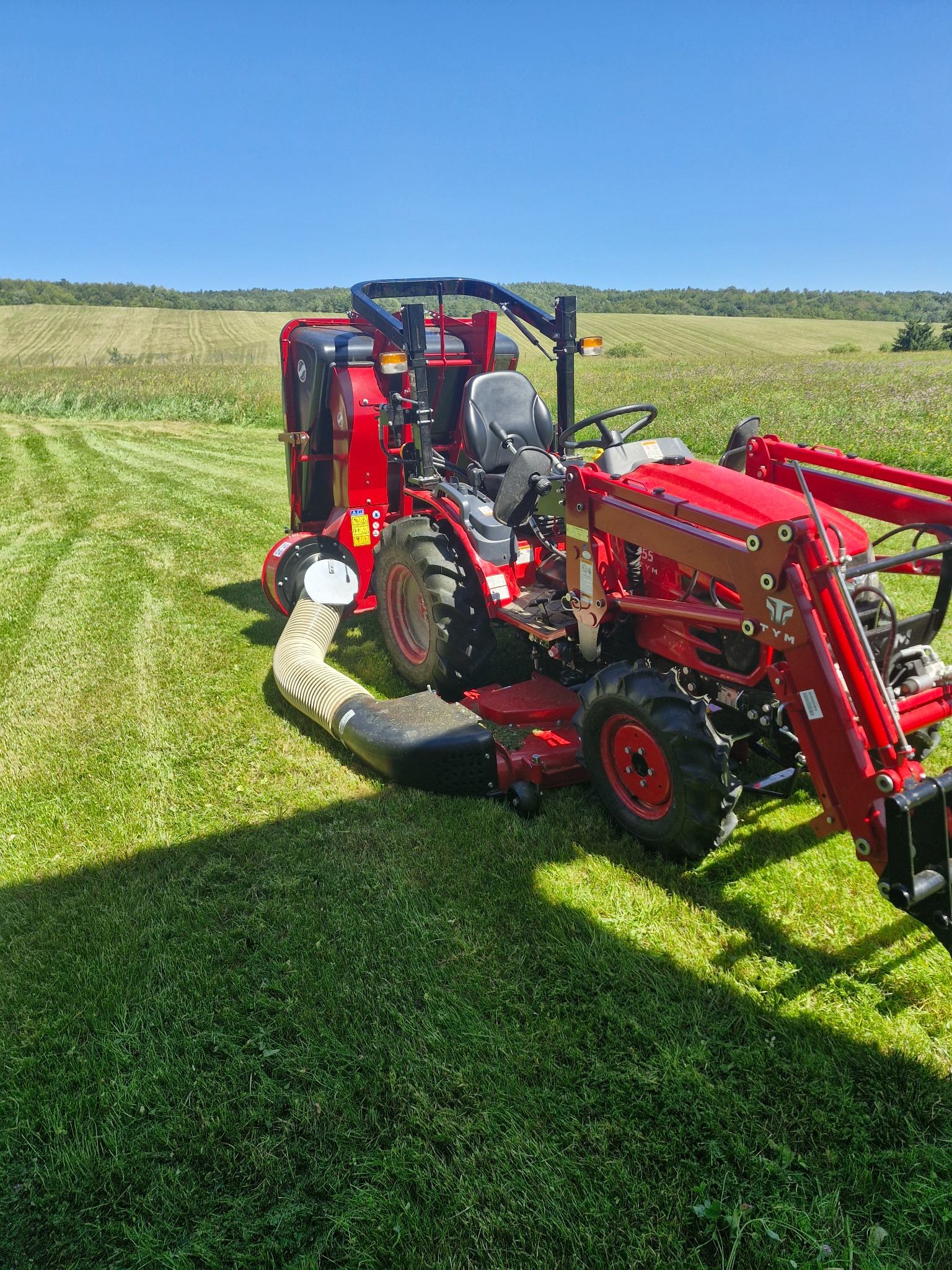 Traktor s kosačkou a zberným košom na pokosenom trávniku