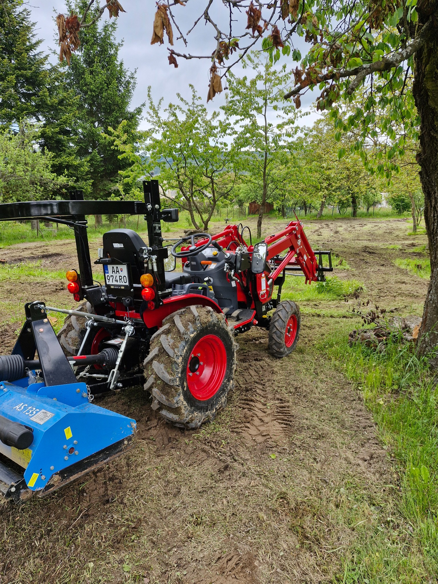 Traktor s mulčovačom na upravenom pozemku medzi stromami