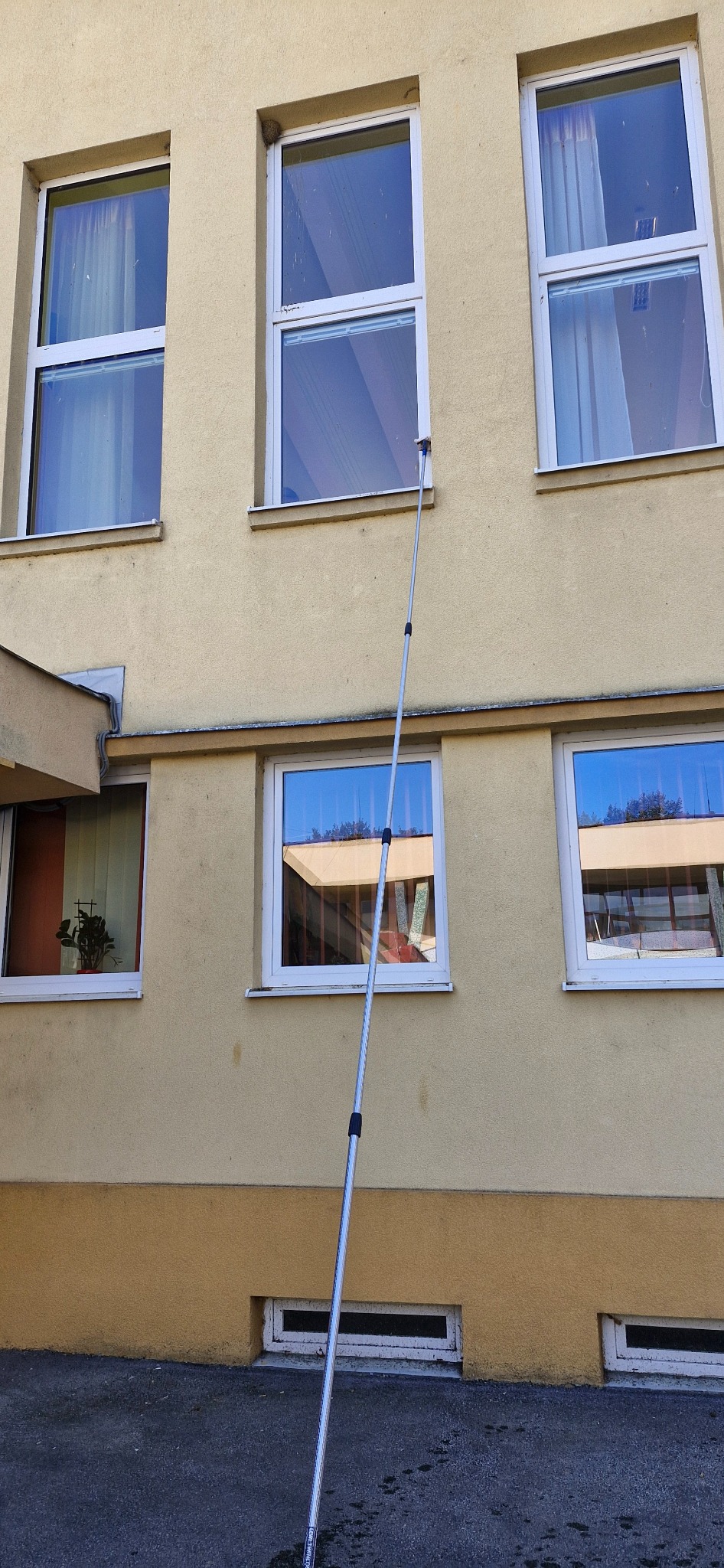 Umývanie okien budovy teleskopickou tyčou zo zeme