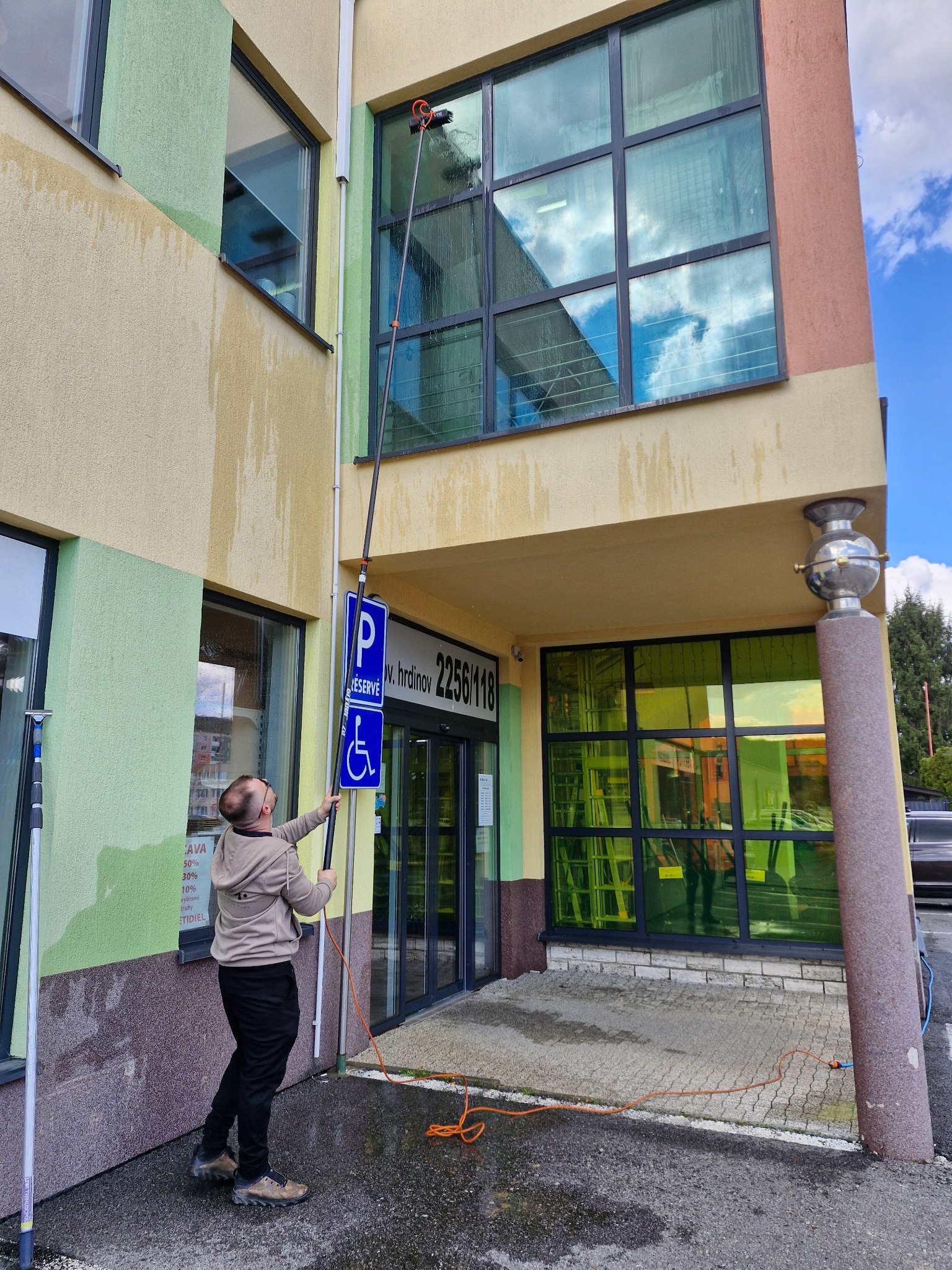Pracovník umývajúci veľké presklenie teleskopickou tyčou zo zeme